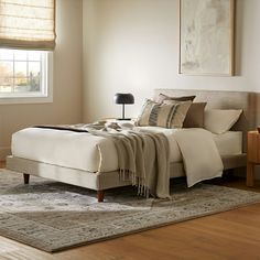 a large bed sitting on top of a wooden floor next to a lamp and window