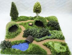 a knitted landscape with trees, bushes and a pond in the middle is shown