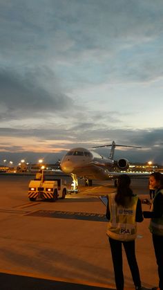 two people standing in front of an airplane on the tarmac at night, talking to each other