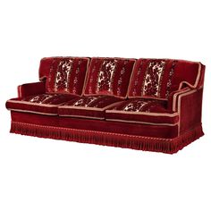 a red velvet couch with fringe trimmings on the arms and back, sitting in front of a white background