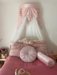 a bed with pink comforter and pillows on top of it next to a bottle of perfume