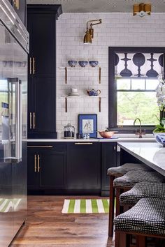 a kitchen with black cabinets and white tile backsplash, wooden flooring and stools