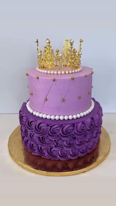 a three tiered cake with purple icing and gold crown on top, sitting on a plate