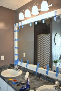 a bathroom sink with blue tape on the mirror and light fixture in the reflection above it