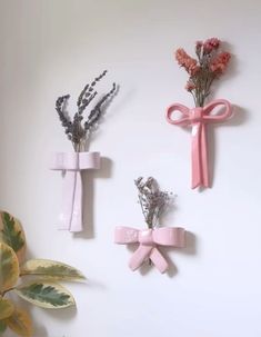 three pink bows and flowers are hanging on the wall next to a potted plant