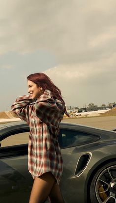 a woman walking next to a car on the road with her hair blowing in the wind