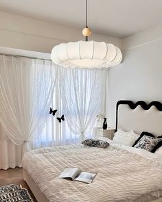 a white bed sitting under a light fixture in a bedroom next to a large window