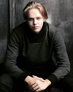 a young man sitting on top of a red chair in front of a black wall