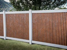 a white fence with brown slats in the grass next to a tree and mountains