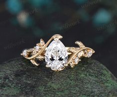 a gold ring with a pear shaped diamond in the center on top of a rock