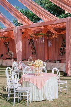 an outdoor wedding reception setup with pink drapes and white chairs, flowers on the table