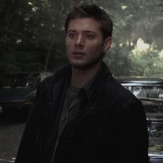 a young man standing in front of parked cars on a rainy day, looking at the camera