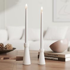 two white candles sitting on top of a wooden table next to a book and bowl