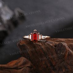 a red and white diamond ring sitting on top of a wooden piece with rocks in the background