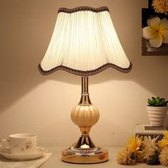 a table lamp sitting on top of a desk next to a cup and saucer