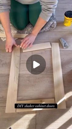 a woman kneeling down on the floor making a frame for a wooden wall art project