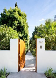 an entrance to a white house with wooden doors and numbers on the side walk, surrounded by greenery