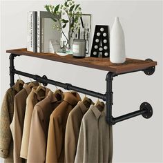 an iron pipe shelf with clothes hanging from it's sides and a vase on top