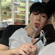 two young men sitting at a table with forks in their mouths