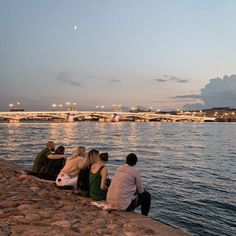 people sitting on the edge of a river watching the sunset