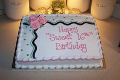 a birthday cake with pink flowers on it sitting on a table next to jars and candles