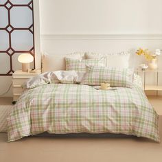 a bed with plaid sheets and pillows in a white room next to a lamp on a table