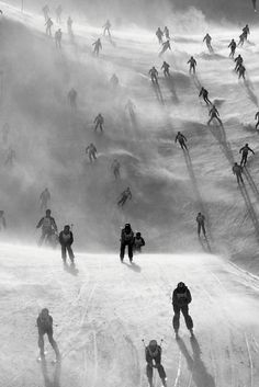 a group of people skiing down a snow covered slope in black and white, surrounded by fog