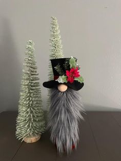 two small christmas trees are next to a gnome's head in a top hat