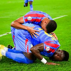 two soccer players are hugging each other on the field in front of another player who is kneeling down