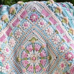 a crocheted pillow is sitting on the ground next to some grass and flowers