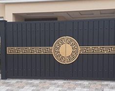 a black gate with a gold design on it in front of a brick driveway area