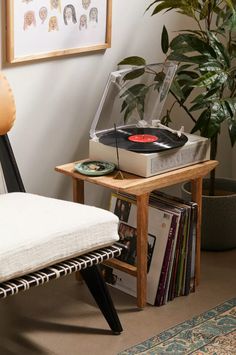 a record player sitting on top of a wooden table next to a chair and potted plant