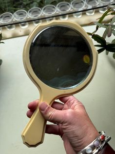 a hand holding a magnifying glass in front of a potted plant on a table