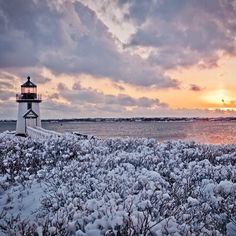 a light house sitting on top of a snow covered field next to the ocean at sunset