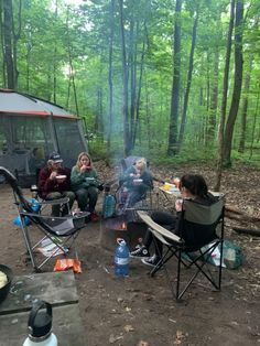 group of people sitting around a campfire in the woods eating food and drinking water