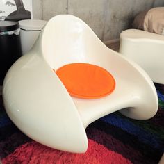 a white chair with an orange seat sitting on top of a colorful rug in a room