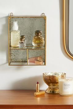 a mirror and some bottles on a wooden table next to a gold shelf with candles