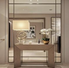 a modern console table with vases and flowers on it in front of a mirror