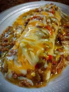 a white plate topped with cheese covered enchilada on top of a table