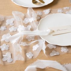 a place setting with white plates and napkins on a wooden table covered in flowers