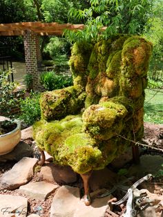 a chair covered in moss sitting on top of a pile of rocks next to a potted plant