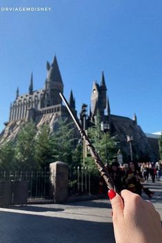 a hand holding a pair of scissors in front of hogwart's castle at universal studios