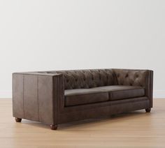 a brown leather couch sitting on top of a hard wood floor next to a white wall