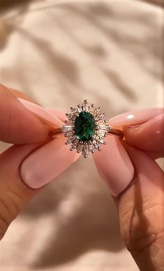 a woman's hand holding a ring with a green stone in the middle of it