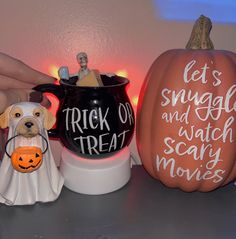 a person holding a mug with a dog in it next to two other halloween decorations