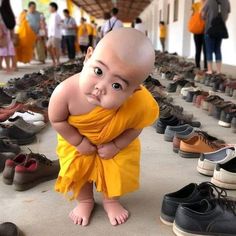 a baby in a yellow dress standing next to many pairs of shoes on the ground