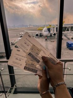 a person holding two tickets in front of an airport terminal with planes on the tarmac