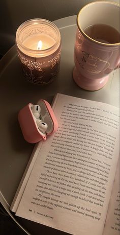 an open book next to a cup of tea and a lit candle on a table