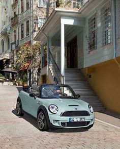 a small blue car parked in front of a building on a brick road with stairs leading up to it