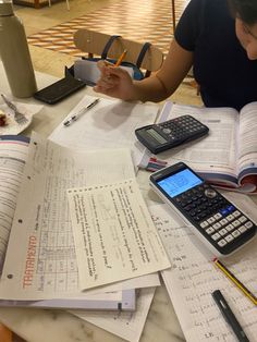 a woman sitting at a table with many papers and calculators on top of it